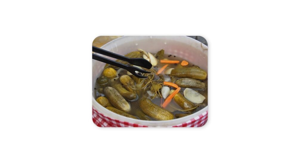 Uborkák ecetes lében, csipesz látható a képben.